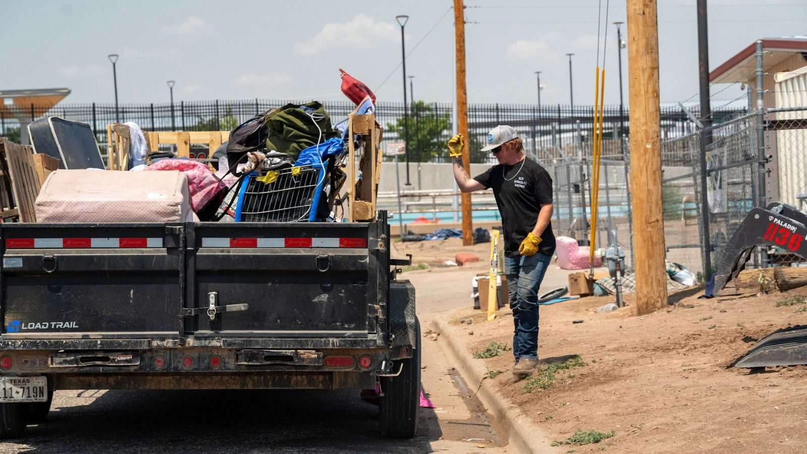 A man wearing gloves beside a trailer filled with mattresses and other items.